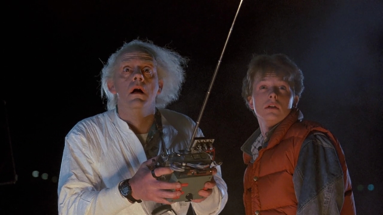Screenshot from Back to the Future, showing mad-scientist Doc and teenaged Marty McFly, standing outside at night, both looking up in concern at something behind the camera.